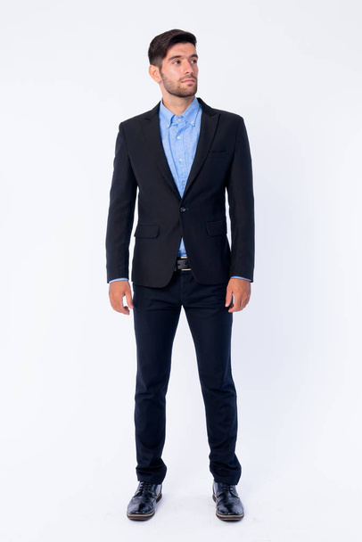 Full body shot of young bearded Persian businessman thinking and looking up - Photo, Image