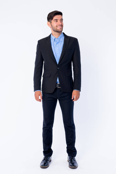 Full body shot of happy young bearded Persian businessman thinking and looking up - Photo, Image