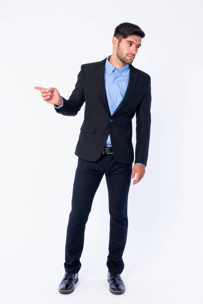 Full body shot of young bearded Persian businessman pointing to side and looking away - Foto, imagen