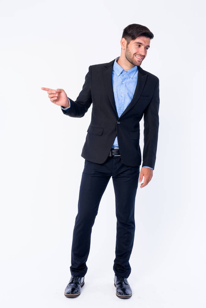 Full body shot of happy young bearded Persian businessman pointing to side and looking away - Photo, Image