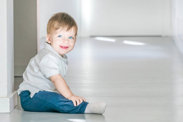 Smiling blue-eyed baby sitting on the floor. - Фото, изображение