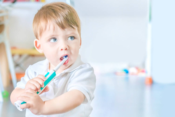 Cute blue-eyed blond baby brushing his teeth with a toothbrush. - Φωτογραφία, εικόνα