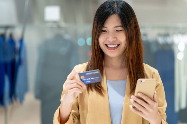 肖像画アジアの女性服ショップ ストアの背景、技術のお金財布とオンライン決済コンセプトでデパートのオンライン ショッピングのスマートな携帯電話でクレジット カードを使用して - 写真・画像