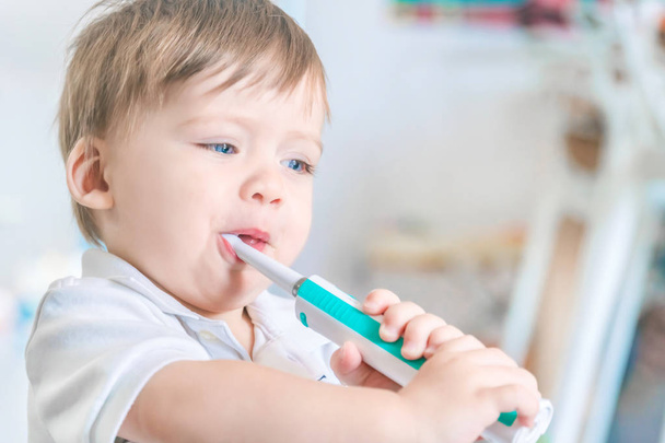 Cute small blue-eyed blond boy brushing his teeth with a toothbr - Foto, afbeelding