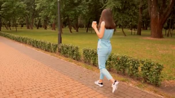 back view young caucasian woman send sound message by mobile walking on the street in city park - Footage, Video