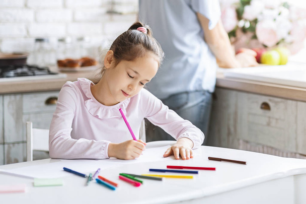 Pretty little girl busy with drawing at kitchen table - Photo, Image