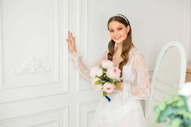 beautiful young woman with makeup and hairstyle in a delicate peignoir with a bouquet in her hand - Photo, image