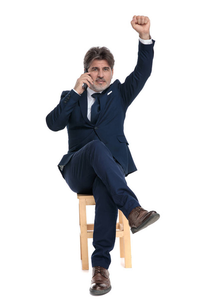 офіційний бізнесмен сидить з кулаком вгору, розмовляючи по телефону
 - Фото, зображення