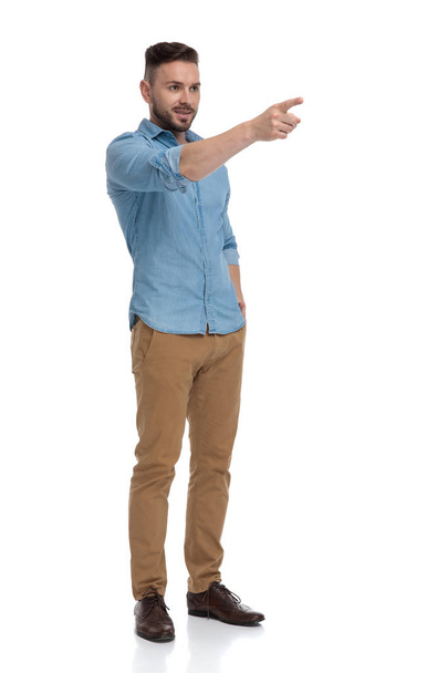casual man with hand in pocket pointing forward - Foto, imagen