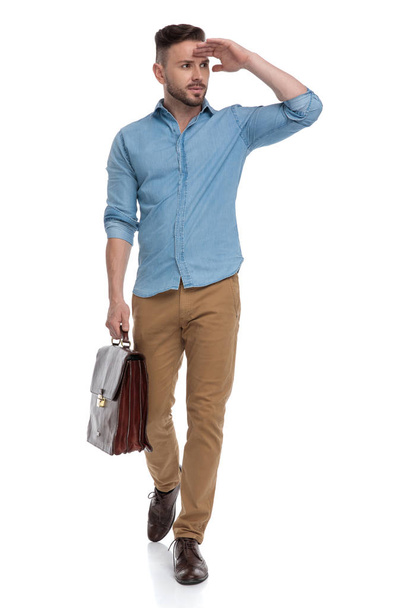 casual man walking with briefcase and looking away vigilant - Фото, изображение