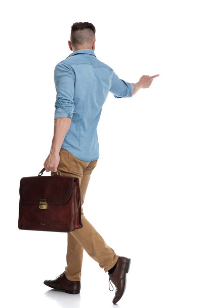ブリーフケースを持つカジュアルな男の歩行と横向きのポインティング - 写真・画像