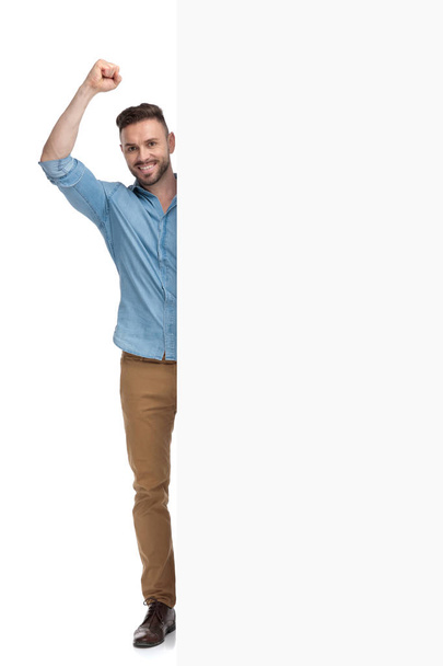 casual man standing behind billboard with fist up - Photo, Image