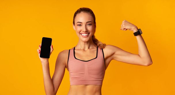 Muchacha sosteniendo Smartphone mostrando músculos sobre fondo amarillo, Mockup, Panorama
 - Foto, imagen
