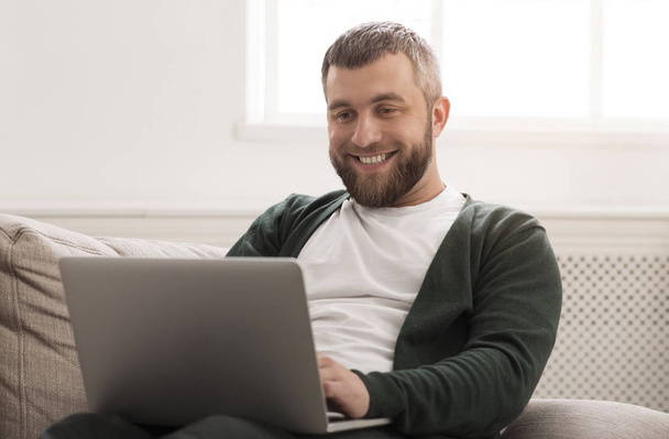 Χαμογελαστός άνθρωπος δουλεύοντας στο laptop σε απευθείας σύνδεση στο σπίτι - Φωτογραφία, εικόνα