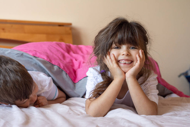 Due fratelli felici che si divertono a letto prima di dormire. Bambini sdraiati sul letto sotto coperta e sorridenti
. - Foto, immagini