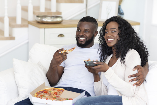 Afrikkalainen amerikkalainen puolisot syövät pizzaa ja katsella televisiota kotona
 - Valokuva, kuva