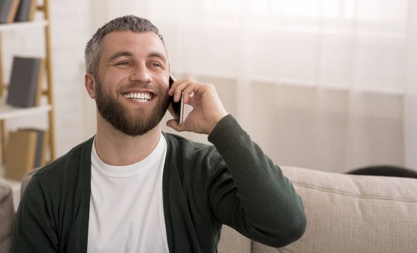 Man talking on mobile phone at home and smiling - Foto, afbeelding
