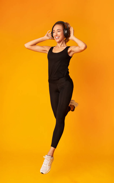 Χαρούμενη γυναίκα στα ακουστικά τρέξιμο στο γυμναστήριο, κίτρινο φόντο - Φωτογραφία, εικόνα