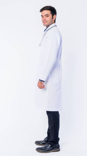 Vista de perfil de plano de cuerpo completo del joven médico persa mirando la cámara
 - Foto, imagen