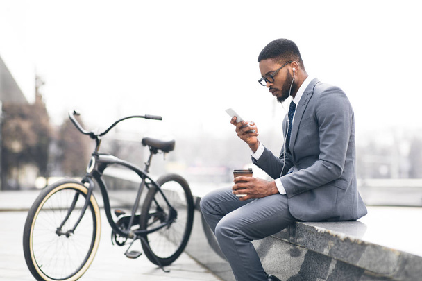 Afro businessman listening music and drinking coffee with bike nearby - Fotoğraf, Görsel