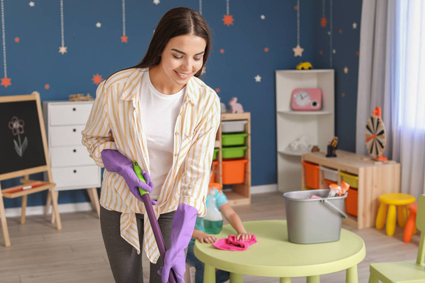 Jovem mulher limpando o quarto da criança
 - Foto, Imagem