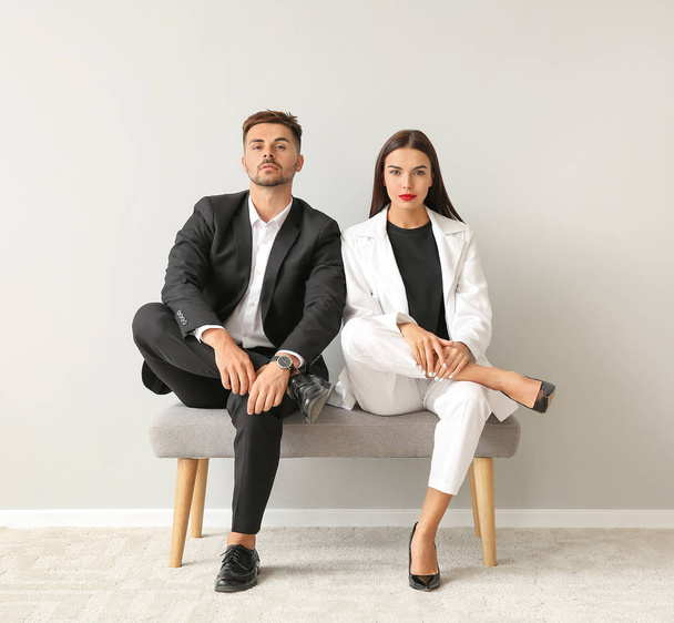 Κομψό νεαρό ζευγάρι κάθεται στο παγκάκι κοντά σε λευκό τοίχο - Φωτογραφία, εικόνα