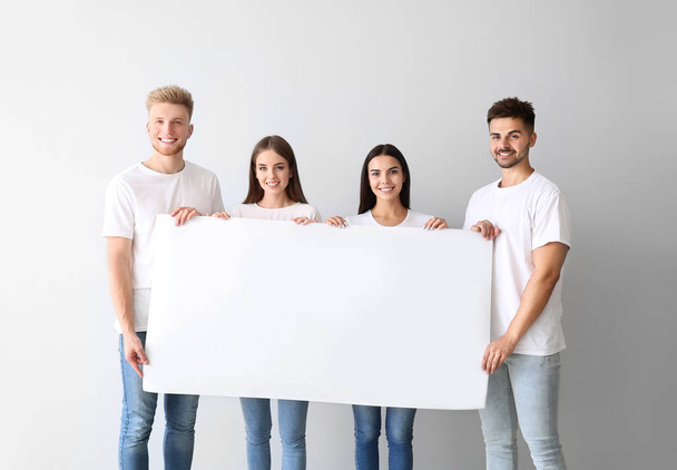 Group of young people in stylish clothes holding blank poster on light background - Foto, Imagen