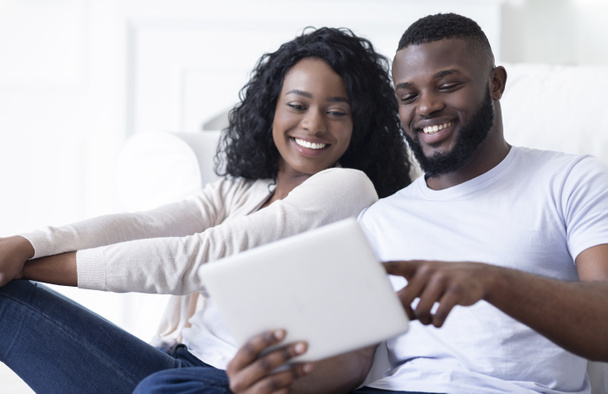 Cheerful african american couple using digital tablet watching funny videos - Fotó, kép