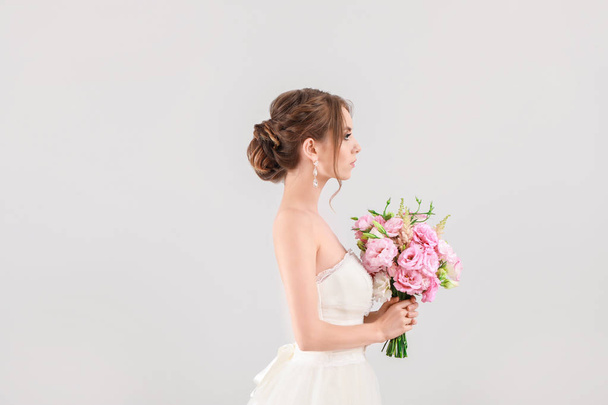 Portrait of beautiful young bride with wedding bouquet on light background - Photo, Image