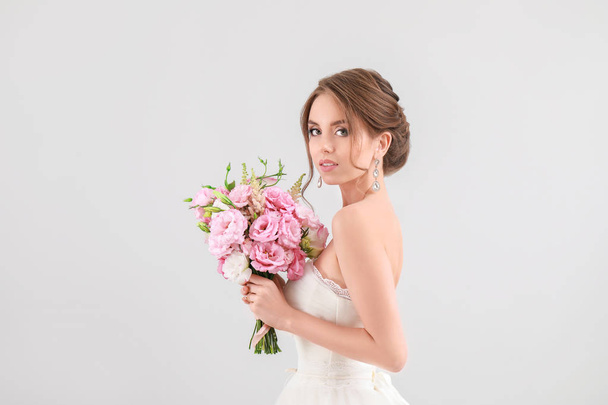 Portrait of beautiful young bride with wedding bouquet on light background - Photo, Image