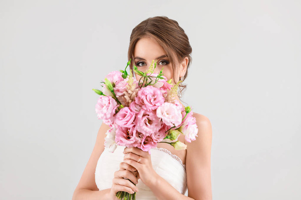 Portrait of beautiful young bride with wedding bouquet on light background - Foto, Bild