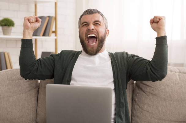 Emocionado hombre barbudo celebrando el éxito delante de la computadora portátil
 - Foto, imagen
