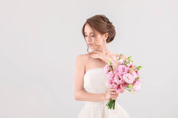 Porträt der schönen jungen Braut mit Brautstrauß auf hellem Hintergrund - Foto, Bild