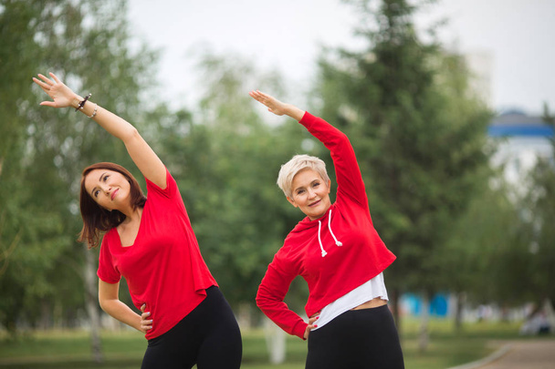 two adult women in sportswear doing exercises in the park in summer - Fotó, kép