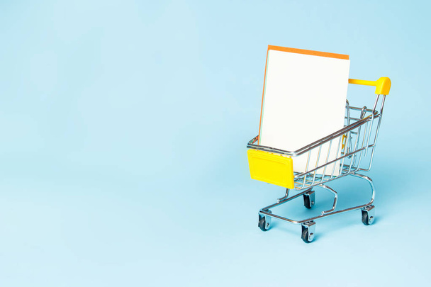 Shopping cart with shop list on blue background. Supermarket trolley as sale, discount. Copy space - Foto, imagen