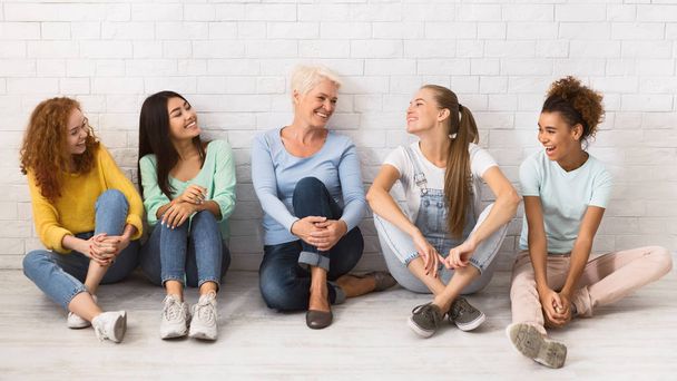 Diverse Ladies Relaxing On Floor Next To White Wall, Panorama - 写真・画像