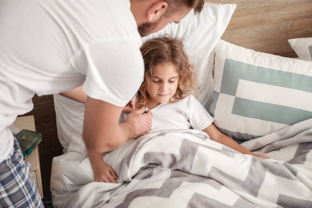 自宅でインフルエンザにかかっている小さな娘の体温を測定する父 - 写真・画像