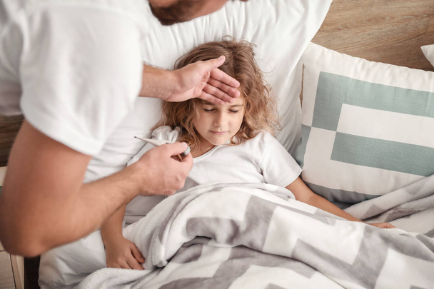 Vader meet de temperatuur van zijn kleine dochter ziek met griep thuis - Foto, afbeelding