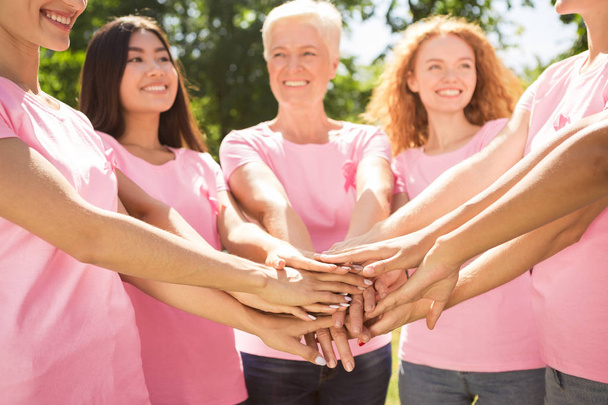 Diversas mujeres que usan camisetas de cinta de cáncer de mama que sostienen las manos
 - Foto, imagen
