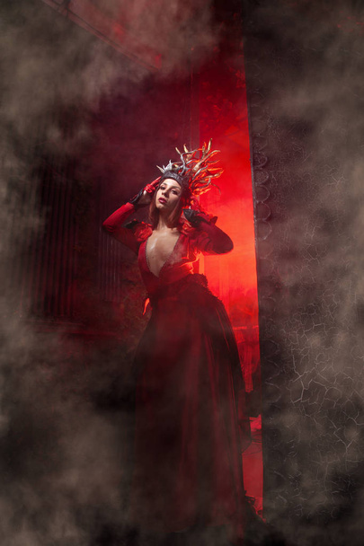 kırmızı duman ile büyük bir kapının arka planda uzun lüks bir elbise ağaç kökleri şeklinde boynuzları ile güzel moda cadı kadın. Cadılar Bayramı konsepti - Fotoğraf, Görsel