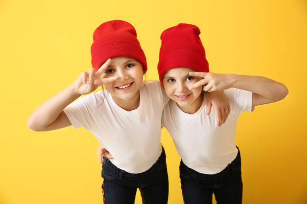 Portrait de jolies jumelles montrant un geste de victoire sur fond de couleur - Photo, image
