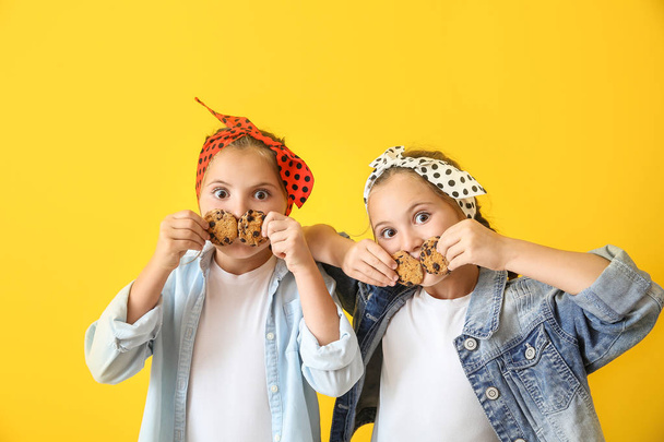 Портрет смешных девочек-близнецов с печеньем на цветном фоне
 - Фото, изображение