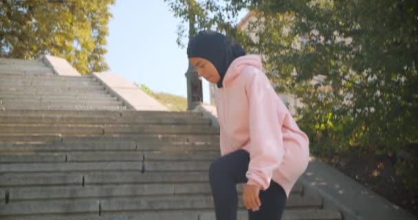 Nahaufnahme Porträt eines jungen attraktiven afrikanisch-amerikanischen muslimischen Mädchens im Hijab, das auf Treppen in urbanen Städten im Freien stürzt - Filmmaterial, Video