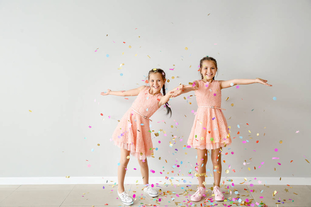 Portrait of happy twin girls with falling confetti near light wall - Foto, Imagem
