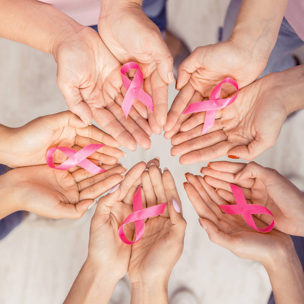 Las manos femeninas se unieron en círculo sosteniendo cintas rosadas, fondo blanco
 - Foto, imagen