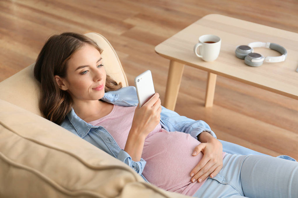 Красива вагітна жінка з мобільним телефоном лежить на дивані вдома
 - Фото, зображення