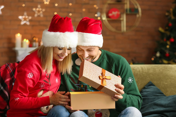 Happy couple in Santa hats and with Christmas gift at home - Foto, Imagen