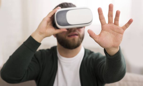 Man met behulp van VR-bril thuis, kijkend naar zijn hand - Foto, afbeelding