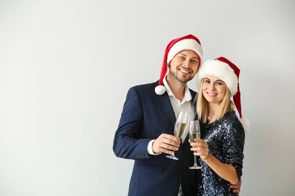 Happy couple in Santa hats drinking champagne on light background - Valokuva, kuva