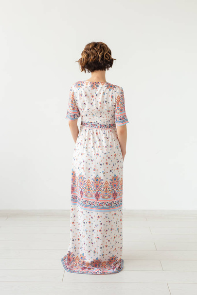 Hátulnézet egy fiatal karcsú nő egy hosszú mintás ruhát állt szemben egy fehér falat. Az egyedi termékek koncepciója - Fotó, kép